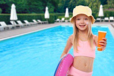 Image of Cute little girl with tube of sunscreen and inflatable ring by outdoor swimming pool. Sun protection product on her cheek