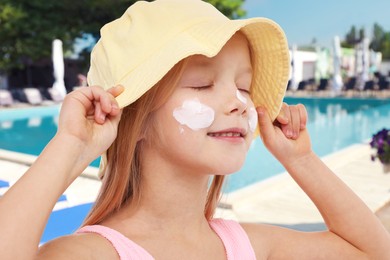 Image of Cute little girl with sun protection product on her cheek by outdoor swimming pool