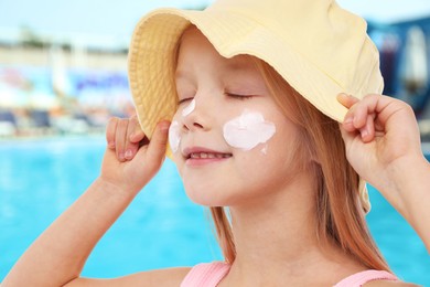 Image of Cute little girl with sun protection product on her cheek by outdoor swimming pool