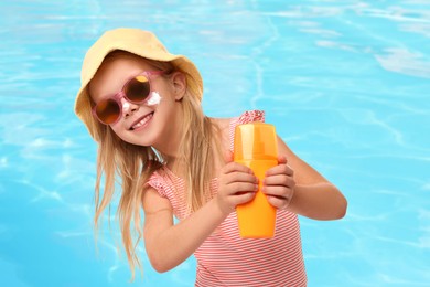 Image of Cute little girl with bottle of sunscreen by outdoor swimming pool. Sun protection product on her cheek