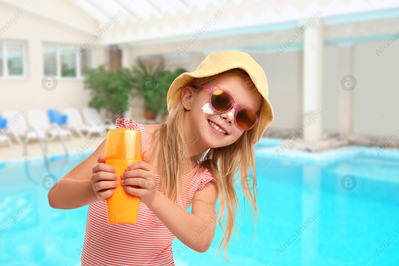 Image of Cute little girl with bottle of sunscreen by swimming pool. Sun protection product on her cheek