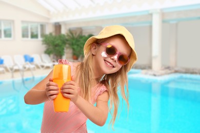 Image of Cute little girl with bottle of sunscreen by swimming pool. Sun protection product on her cheek
