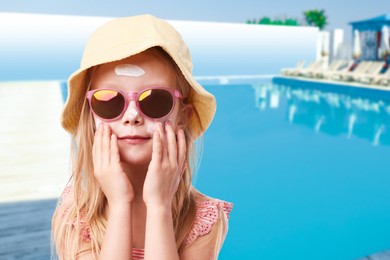 Image of Cute little girl with sun protection product on her cheek by outdoor swimming pool
