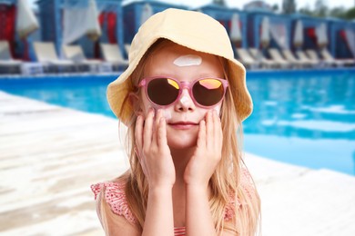 Image of Cute little girl with sun protection product on her cheek by outdoor swimming pool