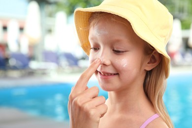 Image of Mother applying sun protection product on her daughter's nose by outdoor swimming pool, closeup