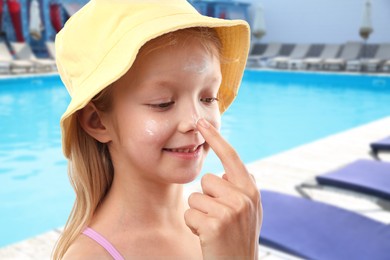Image of Mother applying sun protection product on her daughter's nose by outdoor swimming pool, closeup