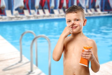 Image of Little boy applying sun protection product on his face by outdoor swimming pool