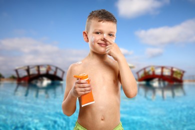 Image of Little boy applying sun protection product on his face by outdoor swimming pool