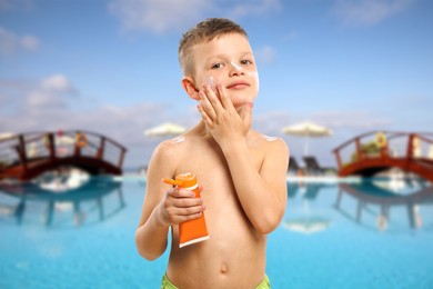 Image of Little boy applying sun protection product on his face by outdoor swimming pool