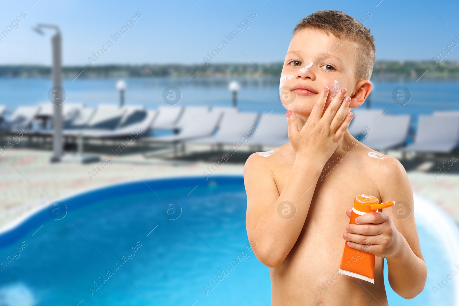 Image of Little boy applying sun protection product on his face by outdoor swimming pool