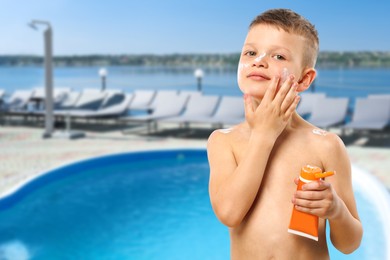 Image of Little boy applying sun protection product on his face by outdoor swimming pool