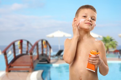 Image of Little boy applying sun protection product on his face by outdoor swimming pool