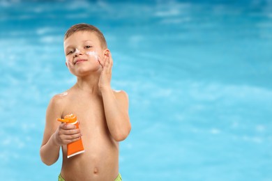 Image of Little boy applying sun protection product on his face by outdoor swimming pool