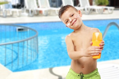 Image of Little boy with bottle of sunscreen by outdoor swimming pool. Sun protection product on his skin