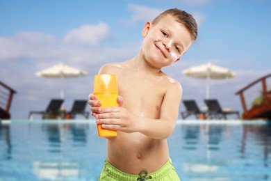 Image of Little boy with bottle of sunscreen by outdoor swimming pool. Sun protection product on his skin