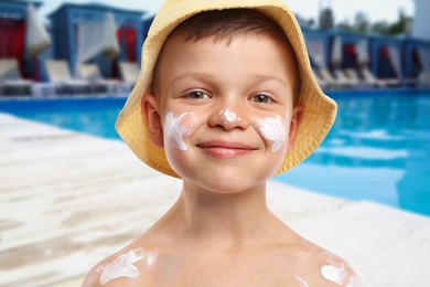 Image of Little boy with sun protection product on his skin by outdoor swimming pool