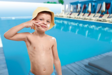 Image of Little boy applying sun protection product on his face by outdoor swimming pool