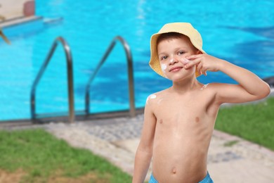 Image of Little boy applying sun protection product on his face by outdoor swimming pool