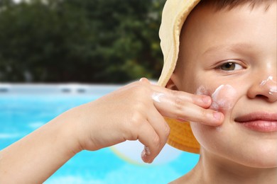Image of Little boy applying sun protection product on his face by outdoor swimming pool, closeup