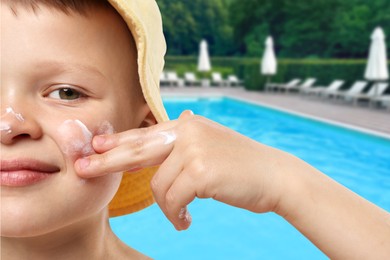 Image of Little boy applying sun protection product on his face by outdoor swimming pool, closeup
