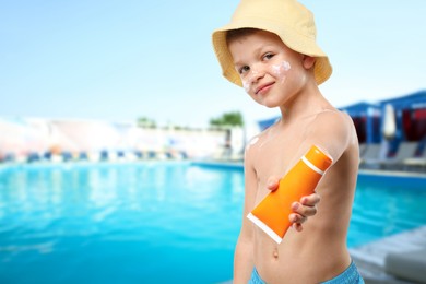 Image of Little boy with tube of sunscreen by outdoor swimming pool. Sun protection product on his skin