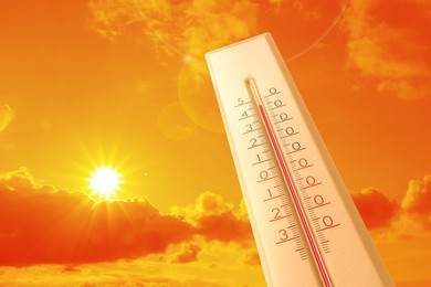 Image of Extremely high temperature on thermometer against orange sky on sunny day. Severely hot summer weather