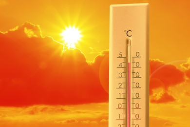 Image of Extremely high temperature on thermometer against orange sky on sunny day. Severely hot summer weather