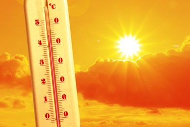 Image of Extremely high temperature on thermometer against orange sky on sunny day. Severely hot summer weather