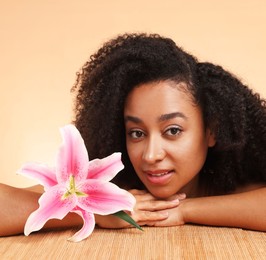 Photo of Portrait of beautiful Brazilian woman with lily flower after spa treatment at bamboo table on beige background, closeup
