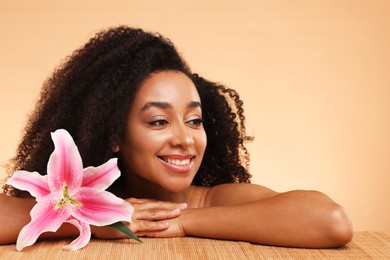Photo of Portrait of beautiful Brazilian woman with lily flower after spa treatment at bamboo table on beige background