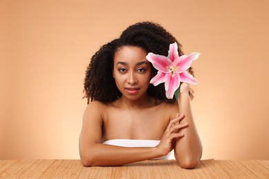 Photo of Portrait of beautiful Brazilian woman with lily flower after spa treatment at bamboo table on beige background