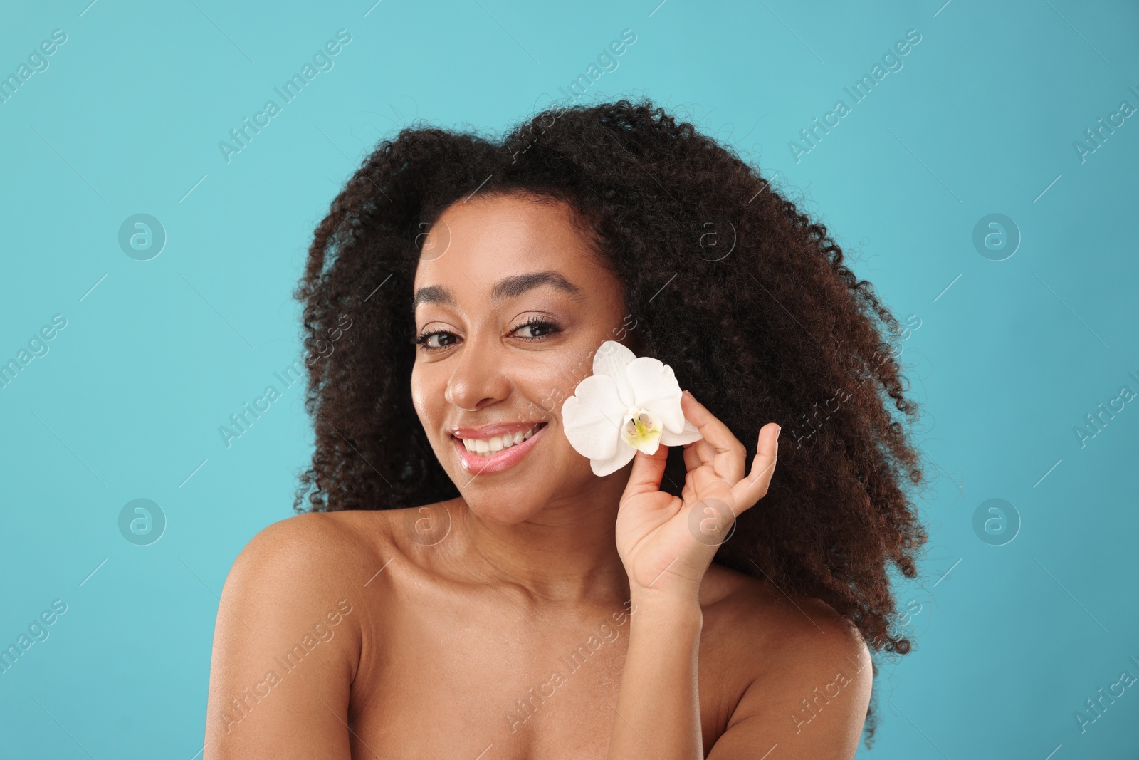 Portrait of beautiful Brazilian woman with orchid flower after spa treatment on light blue background Photo of Portrait of beautiful Brazilian woman with orchid flower after spa treatment on light blue background