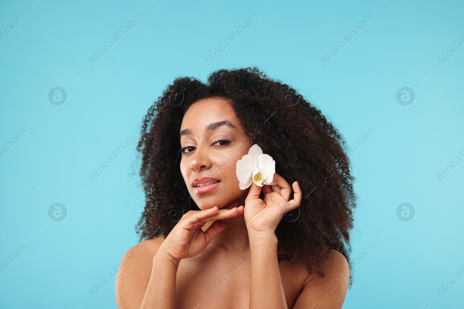 Portrait of beautiful Brazilian woman with orchid flower after spa treatment on light blue background Photo of Portrait of beautiful Brazilian woman with orchid flower after spa treatment on light blue background