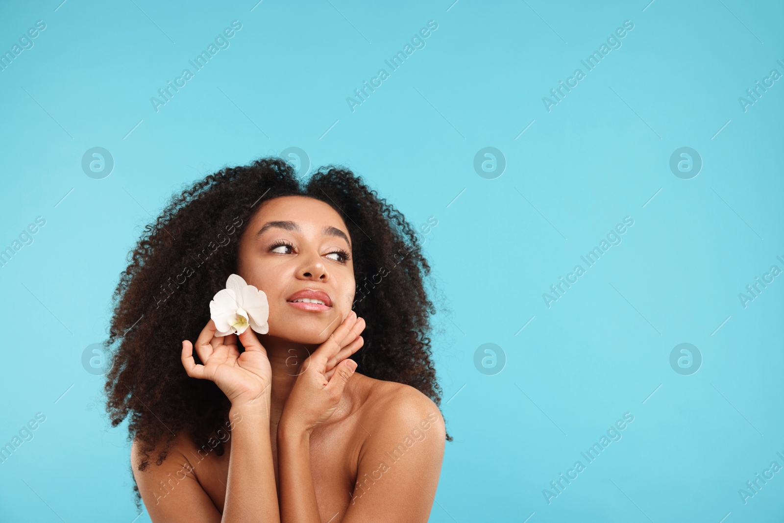Portrait of beautiful Brazilian woman with orchid flower after spa treatment on light blue background. Space for text Photo of Portrait of beautiful Brazilian woman with orchid flower after spa treatment on light blue background. Space for text