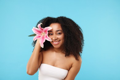 Photo of Portrait of beautiful Brazilian woman with lily flower after spa treatment on light blue background