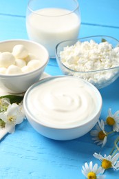 Photo of Different fresh dairy products and flowers on light blue wooden table, closeup