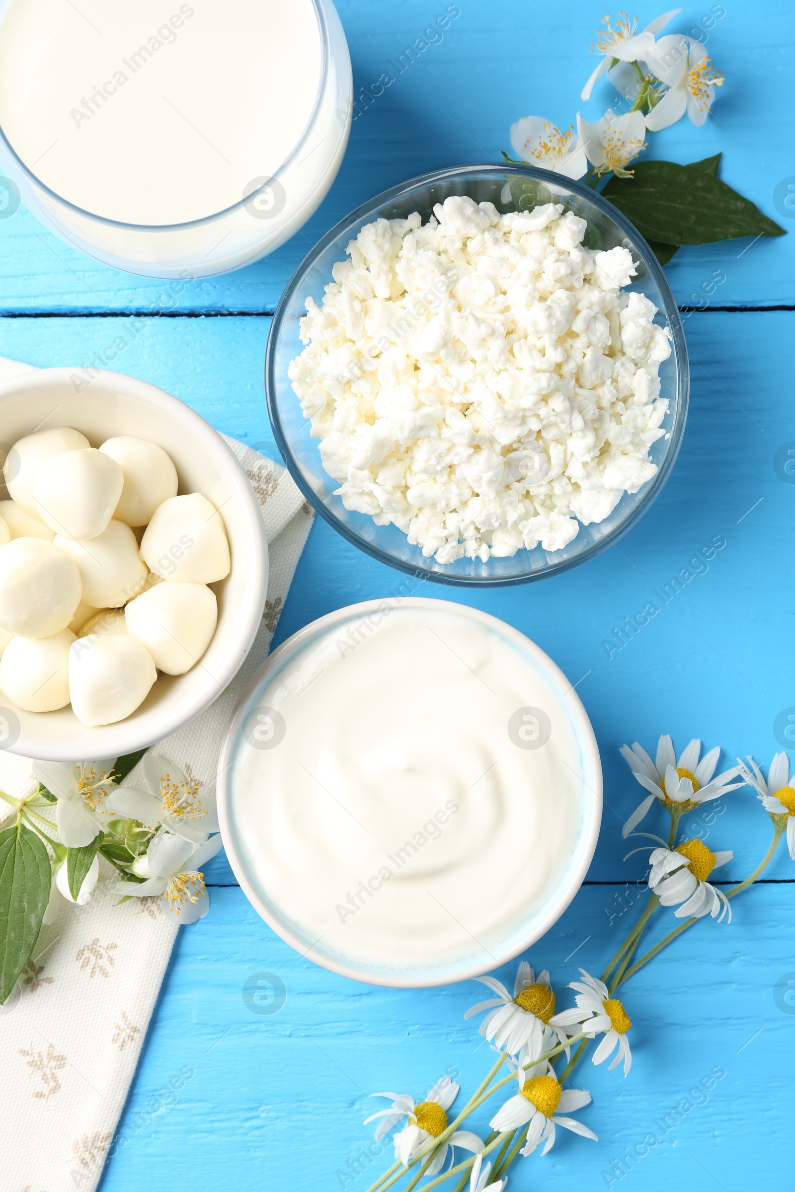 Photo of Different fresh dairy products and flowers on light blue wooden table, flat lay