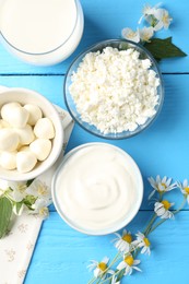Photo of Different fresh dairy products and flowers on light blue wooden table, flat lay
