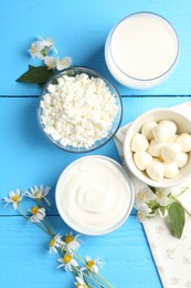 Photo of Different fresh dairy products and flowers on light blue wooden table, flat lay