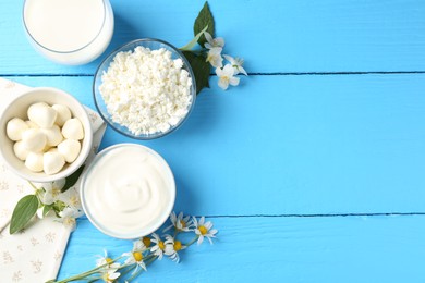 Photo of Different fresh dairy products and flowers on light blue wooden table, flat lay. Space for text