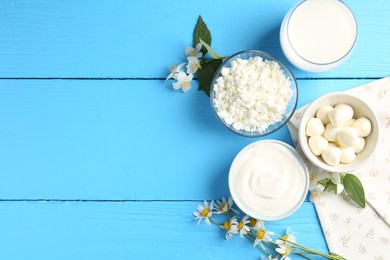 Photo of Different fresh dairy products and flowers on light blue wooden table, flat lay. Space for text