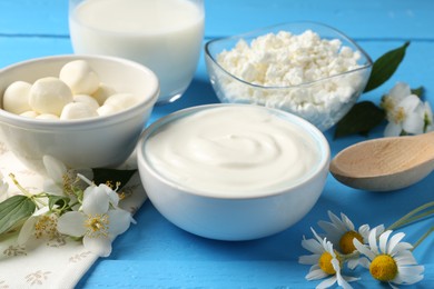 Photo of Different fresh dairy products and flowers on light blue wooden table, closeup