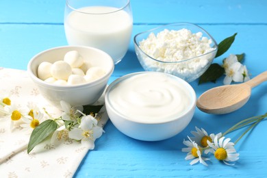 Photo of Different fresh dairy products and flowers on light blue wooden table, closeup