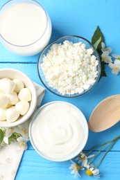 Photo of Different fresh dairy products and flowers on light blue wooden table, flat lay