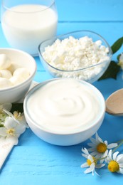 Photo of Different fresh dairy products and flowers on light blue wooden table, closeup
