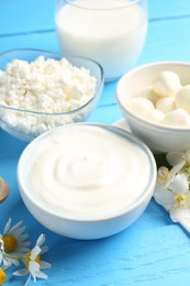 Photo of Different fresh dairy products and flowers on light blue wooden table, closeup
