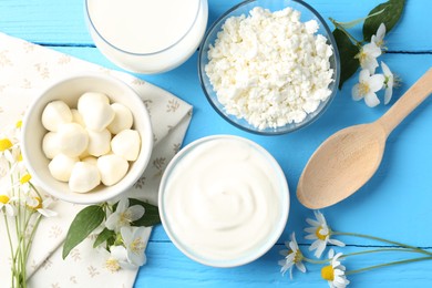 Photo of Different fresh dairy products and flowers on light blue wooden table, flat lay