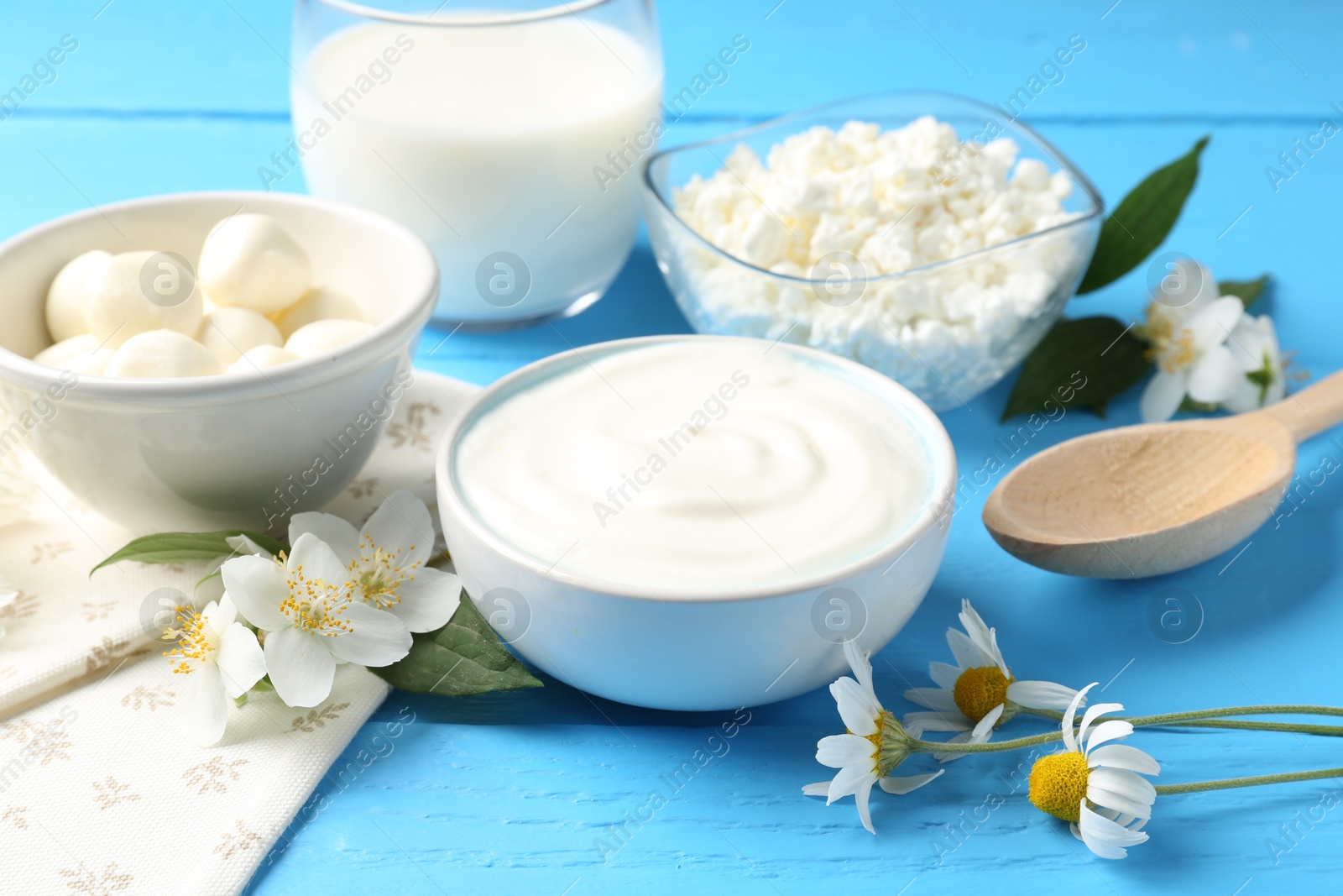 Photo of Different fresh dairy products and flowers on light blue wooden table, closeup