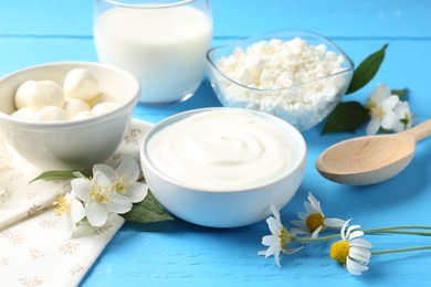 Photo of Different fresh dairy products and flowers on light blue wooden table, closeup