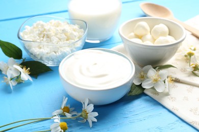 Photo of Different fresh dairy products and flowers on light blue wooden table, closeup